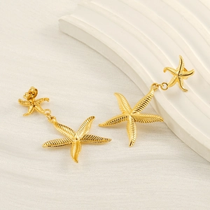 Macro detail of golden starfish earrings set on a textured white coastal surface