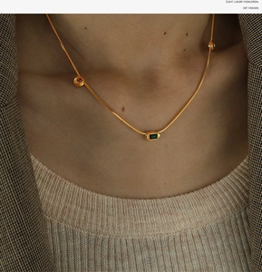 Close-up of a 18K gold snake chain necklace with emerald green and red gemstone pendants