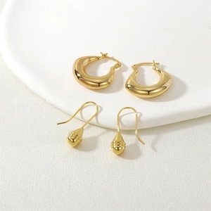 Macro shot of gold hoop earrings and textured conical pendant on a white tray