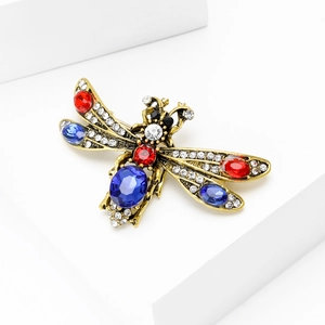 Vintage dragonfly brooch with red and blue crystals on white geometric stand