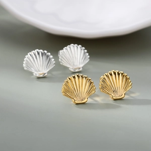Detail of polished scallop shell earrings in gold and silver finish with textured ridges