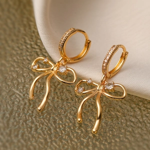 Gold plated bow knot hoop earrings with sparkling cubic zirconia on glass background