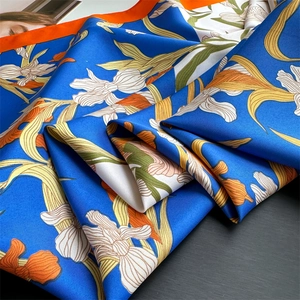 Détail de foulard carré en soie bleue avec fleurs blanches et bordure orange contrastée