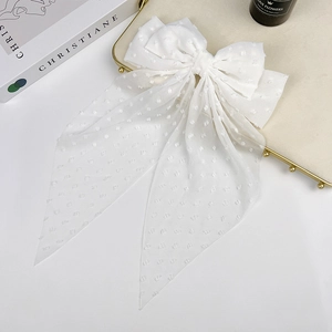 Detail of a large white chiffon bow hair clip with polka dot texture on a golden tray