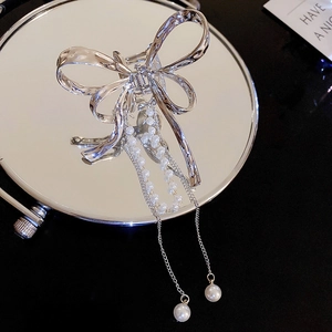 Detailed macro view of silver bow hair clip with elegant long pearl tassel on a mirror