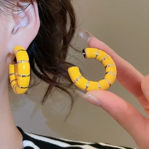 Detailed close-up of yellow enamel C-shaped earrings with gold striped accents