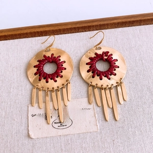 Detail view of ethnic gold alloy hollow earrings with red tassels on rustic texture