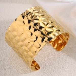 Detailed macro view of gold-tone wide cuff bracelet with hammered metal texture