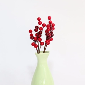 Close-up of artificial red berries in a light green ceramic vase for festive home decor