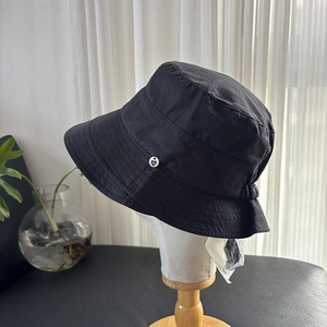 Detail showing the side of a black bucket hat with a heart-shaped metal buckle on the brim