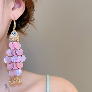 Close-up of a golden fish earring with pink shell scales on a model's ear