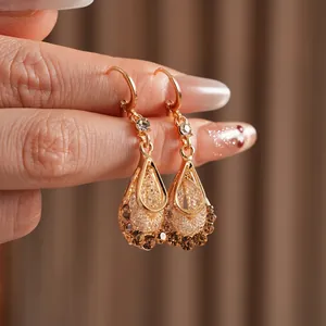 Vintage gold teardrop earrings with crystals and woven texture on warm fabric background