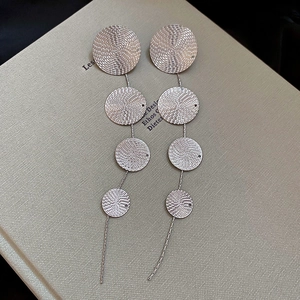 Close-up of silver drop earrings with four textured round discs on a book