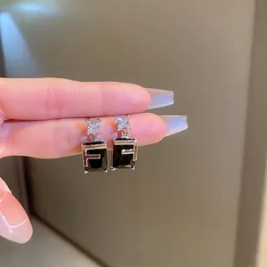 Macro view of geometric silver earrings with black zircon stones and metal F letter