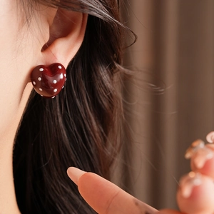 Close-up of model wearing dark red heart-shaped earrings with white polka dots