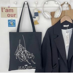 Detail of artistic white cat line drawing and text on black canvas tote bag