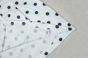 Detailed close-up of double-stitched hem on white polka dot fabric for mini dress