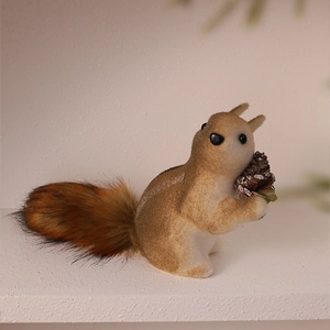 Detailed view of a small flocked squirrel ornament holding a cone for festive decoration