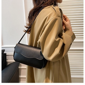 Close-up of black retro shoulder bag with wave edge flap styled with a beige trench coat