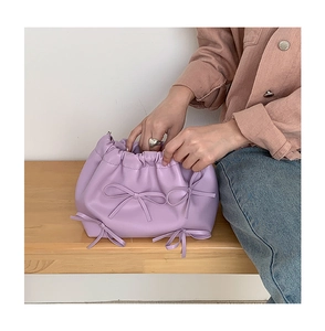 Close-up of lavender pleated handbag with decorative bows on a wooden bench