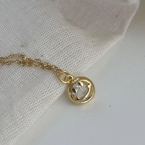 Close-up of gold chain necklace featuring a round smiley face zircon pendant on white linen