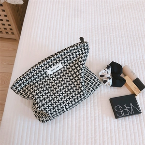 Detail of checkered jacquard fabric storage bag with zipper and brand label on white bedding
