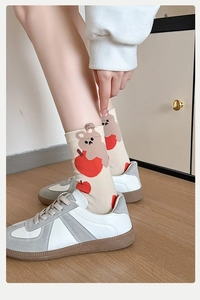 Close-up of cream knit mid-calf socks with red apple and brown bear cartoon patterns