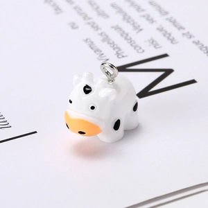 Close-up of a cute resin cow charm with black spots and a silver metal ring for DIY jewelry