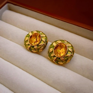 Macro shot of gold-plated vintage earrings with green enamel, leaf reliefs and yellow gems