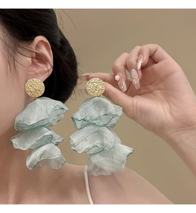 Detail view of large three-layer light green organza flower earrings on female model