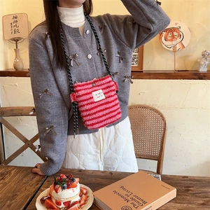 Detail of pink and red striped plush crossbody bag with woven strap in a cozy cafe setting