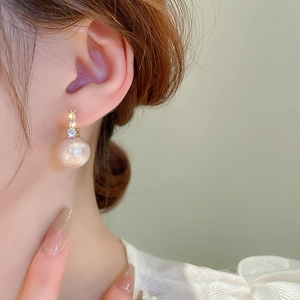 Gros plan de boucles d'oreilles dorées avec zircon et grandes perles blanches élégantes