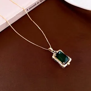 Vintage gold necklace with square green gemstone and zircon accents on brown background