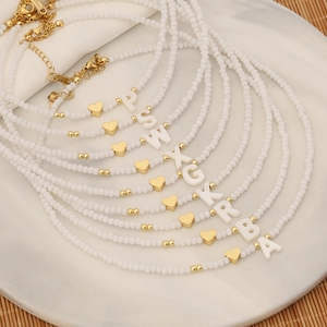 Macro detail of white bead necklaces with gold heart charms and stainless steel clasps