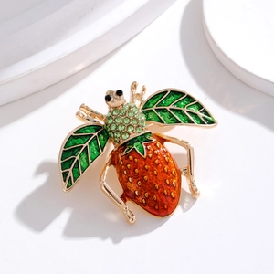 Détail macro d'une broche insecte fraise avec des ailes vertes et des cristaux brillants