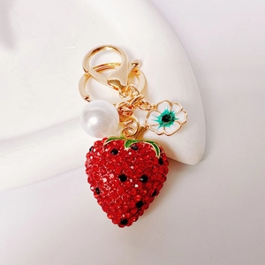Close-up of strawberry keychain with red rhinestones, white pearl and floral charm