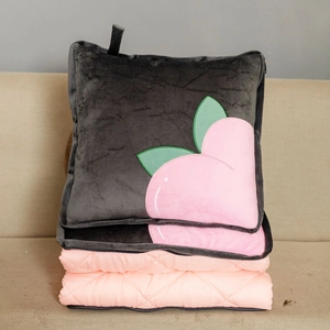 Detail of pink quilted blanket unfolding from a grey cushion with peach embroidery