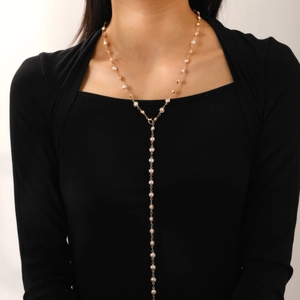 Close-up of golden Y-shaped necklace with small white pearls on a female model