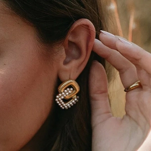 Close-up of gold double rectangle hoop earrings with micro-set pearls worn by a model
