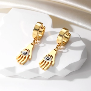 Detail of golden Hamsa Hand earrings with Evil Eye charm on white stone and silk