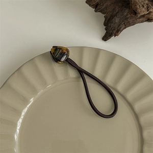Close-up of brown elastic hair tie with amber acetate decorative button in a ceramic tray