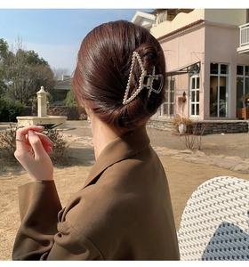 Detail of a hollow triangle metal hair claw clip with pearls worn by a woman outdoors