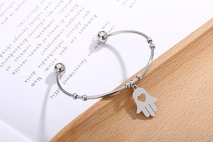 Detail of silver Hamsa hand open bangle with heart charm on vintage book background