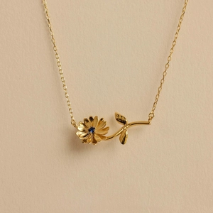 Detail of 18k gold plated daisy pendant necklace featuring a blue gemstone center