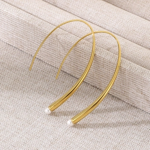 Close-up of golden curved earrings with small white pearls on beige textured fabric