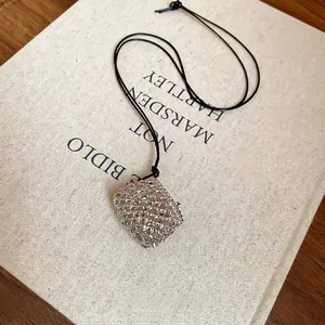 Minimalist wax cord necklace featuring a hollow silver mesh pouch pendant on a book