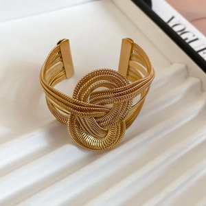 Macro detail of gold-plated twisted metal chain knot on a multi-layer open cuff bracelet