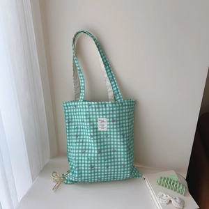 Detail of green plaid cotton tote bag with floral print and inspirational textile label