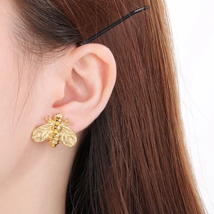 Close-up of a gold bee stud earring worn on ear showing intricate metallic detail
