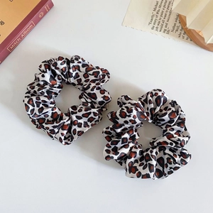Close-up of two silk satin scrunchies featuring classic leopard prints on a white surface